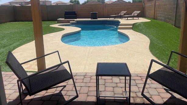 Un patio trasero con piscina, mobiliario de exterior y un muro de ladrillo.