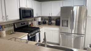 Una cocina moderna con armarios blancos, electrodomésticos de acero inoxidable, una estufa a gas, microondas, refrigerador y cafetera.