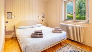 A bedroom with a bed, two bedside tables, a window with a view, and a radiator.