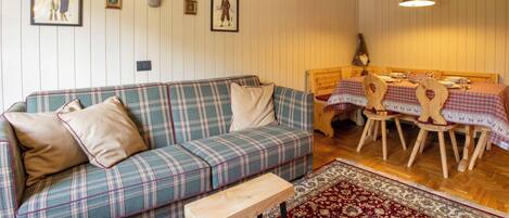 A cozy living room with a plaid sofa, a wooden coffee table, and a dining area with a wooden table and chairs.