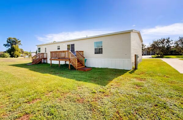 A single-story mobile home with a wooden deck and stairs leading to a front door. - Work and Stay Near the Boat Ramp (Okeechobee)