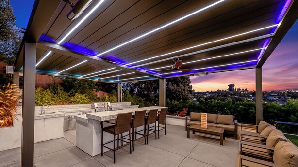An outdoor patio with a bar and seating area, featuring a view of the city skyline at dusk.