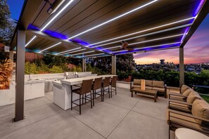 An outdoor patio with a bar and seating area, featuring a view of the city skyline at dusk. - Sunsets & Wine with Panoramic Views San Diego (El Cajon)