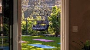A balcony with a hanging chair, yoga mats, and a view of a hilly landscape.