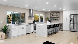 A modern kitchen with white cabinetry, a central island, bar stools, and a stainless steel refrigerator.