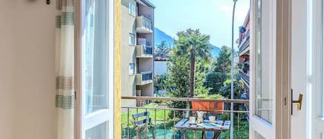 A balcony with a table, chairs, and a view of a residential area with buildings and trees.