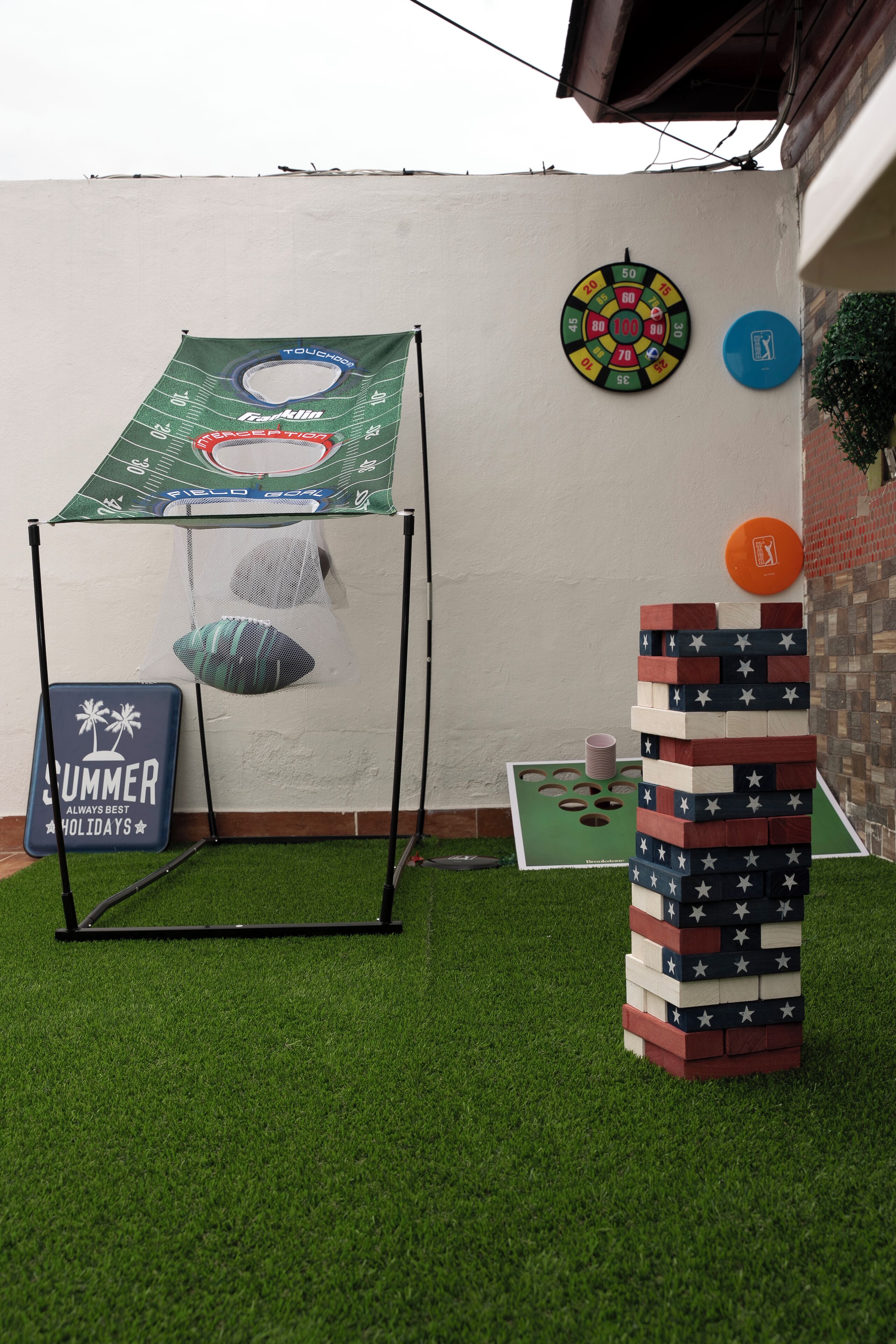 A backyard with artificial grass, a small American flag tower, a baseball tee, and a dartboard.