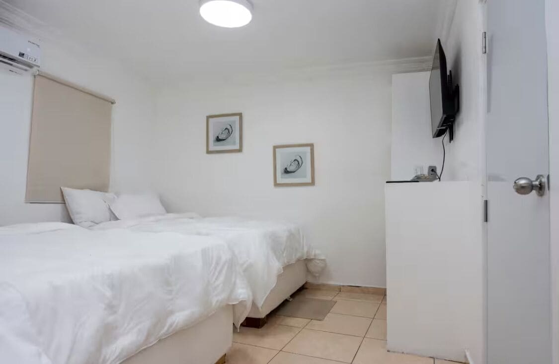 A hotel room with a bed, a television mounted on the wall, and two framed pictures on the wall.