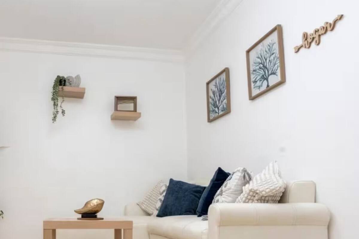 Een moderne woonkamer met een witte bank, een klein houten tafeltje en twee ingelijste kunstwerken aan de muur.