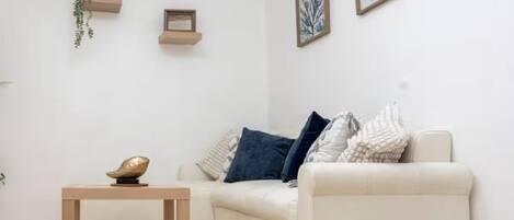Ein modernes Wohnzimmer mit einem weißen Sofa, einem kleinen Holztisch und zwei gerahmten Kunstwerken an der Wand.