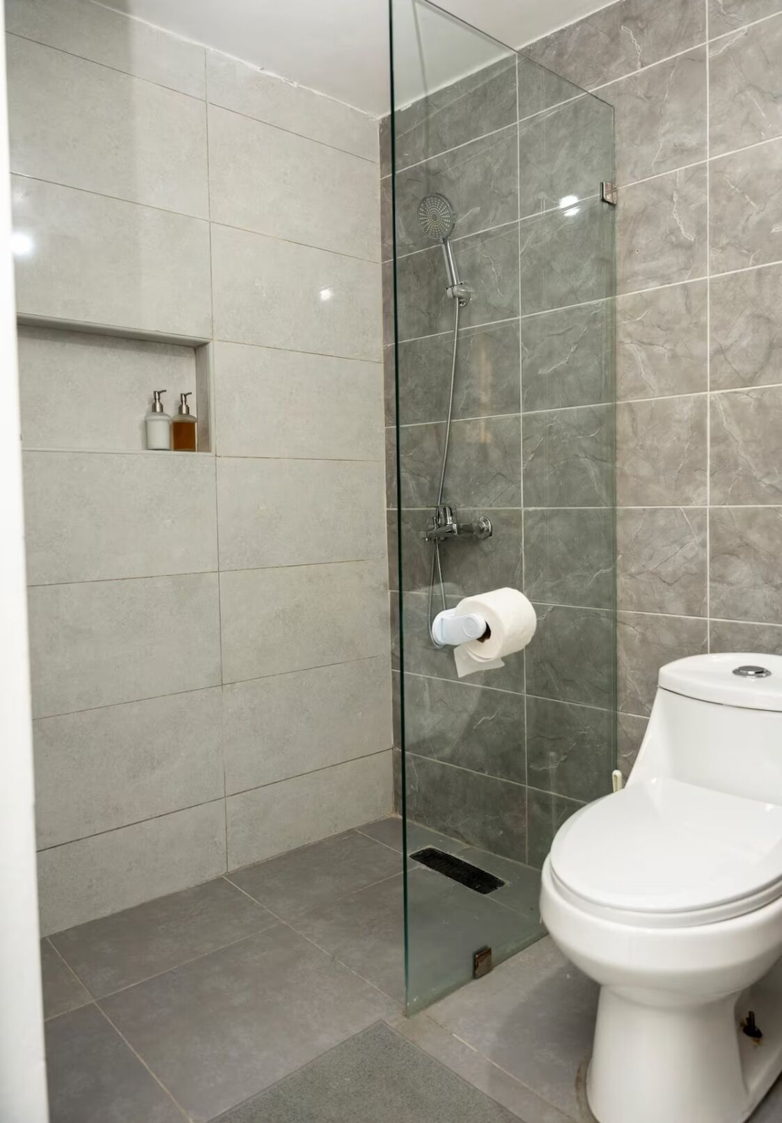 A modern bathroom with a glass-enclosed shower, a toilet, and a shelf with toiletries.