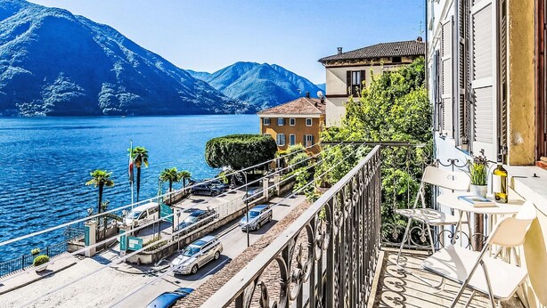 A balcony with a view of a lake and mountains, a parking area, and a building with a balcony. - Martino by Interhome (Argegno)
