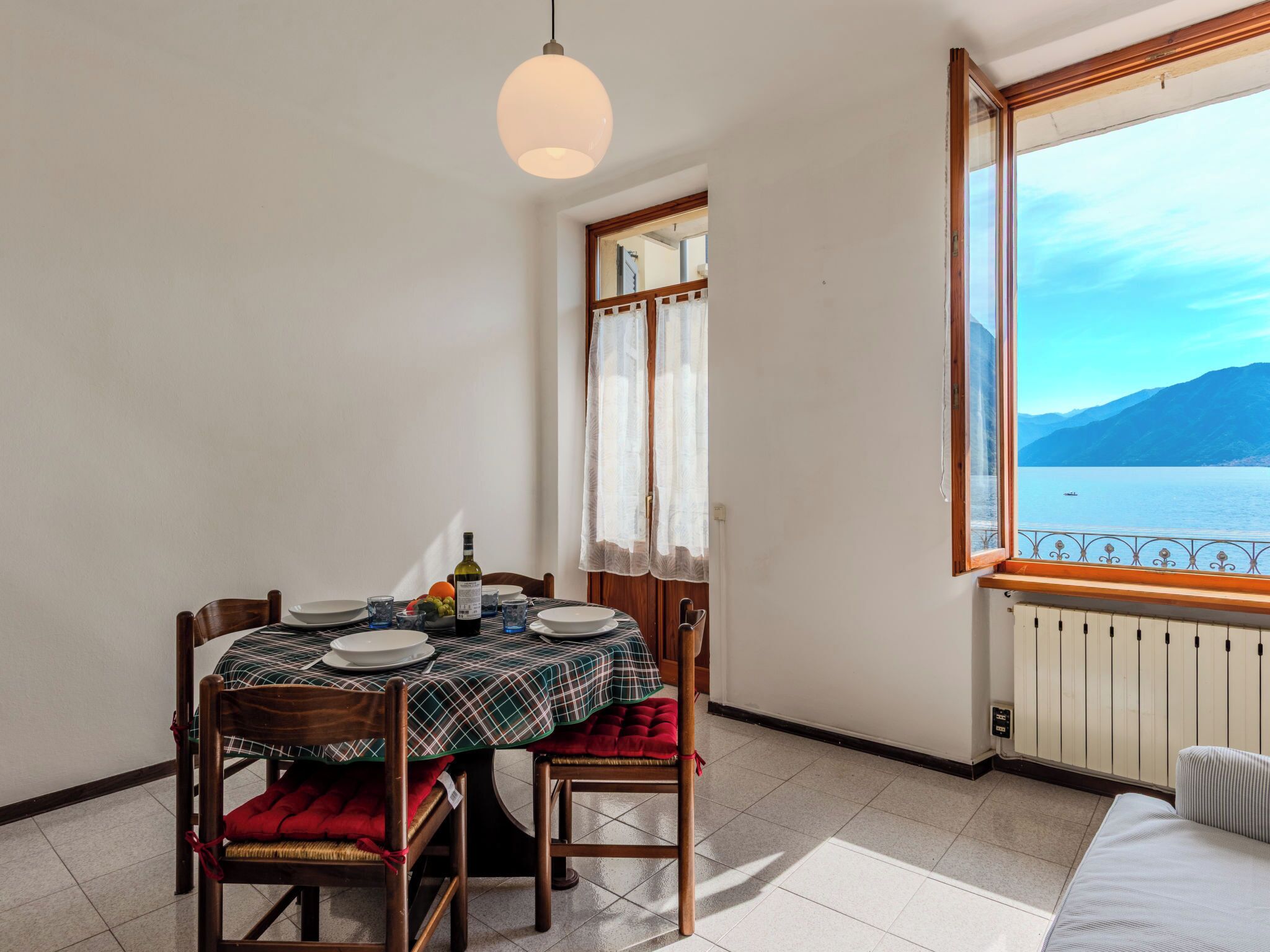 Un coin repas avec une table dressée pour deux personnes, une fenêtre donnant sur un lac et des montagnes, et un radiateur placé sous la fenêtre.