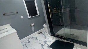 Casa de banho moderna com cabine de duche em vidro, soalho em mármore e toucador branco.
