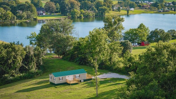 A house with a green roof, surrounded by lush greenery and a lake. - Tiny House with lake view and large yard (McMinnville)