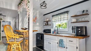 A modern kitchen with white cabinets, a black stove, and a coffee maker. There is a wooden chair and a table with a decorative plant. - Tiny House with lake view and large yard (McMinnville)