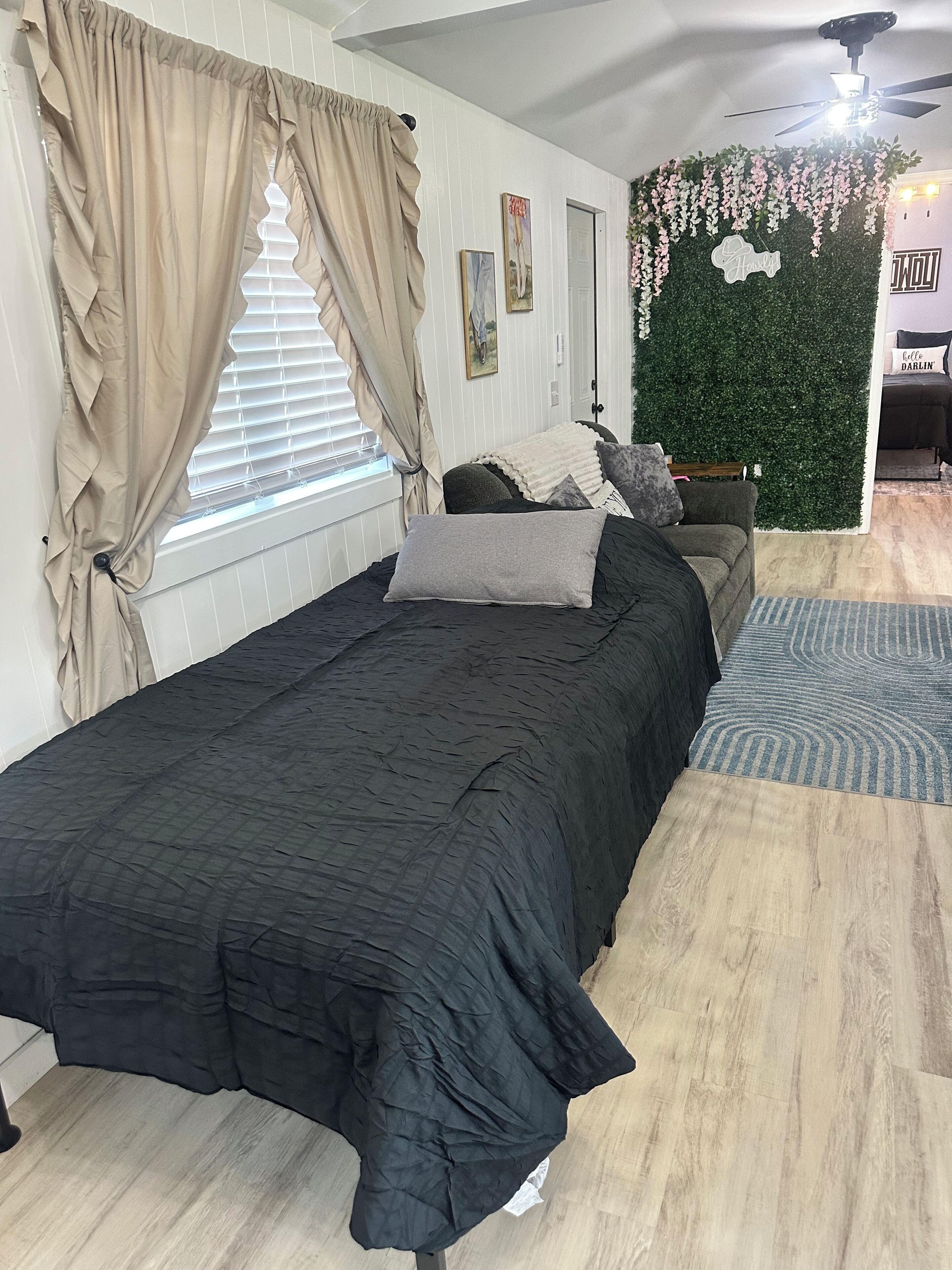 A bedroom with a bed, curtains, a wall-mounted TV, and a green wall decoration.