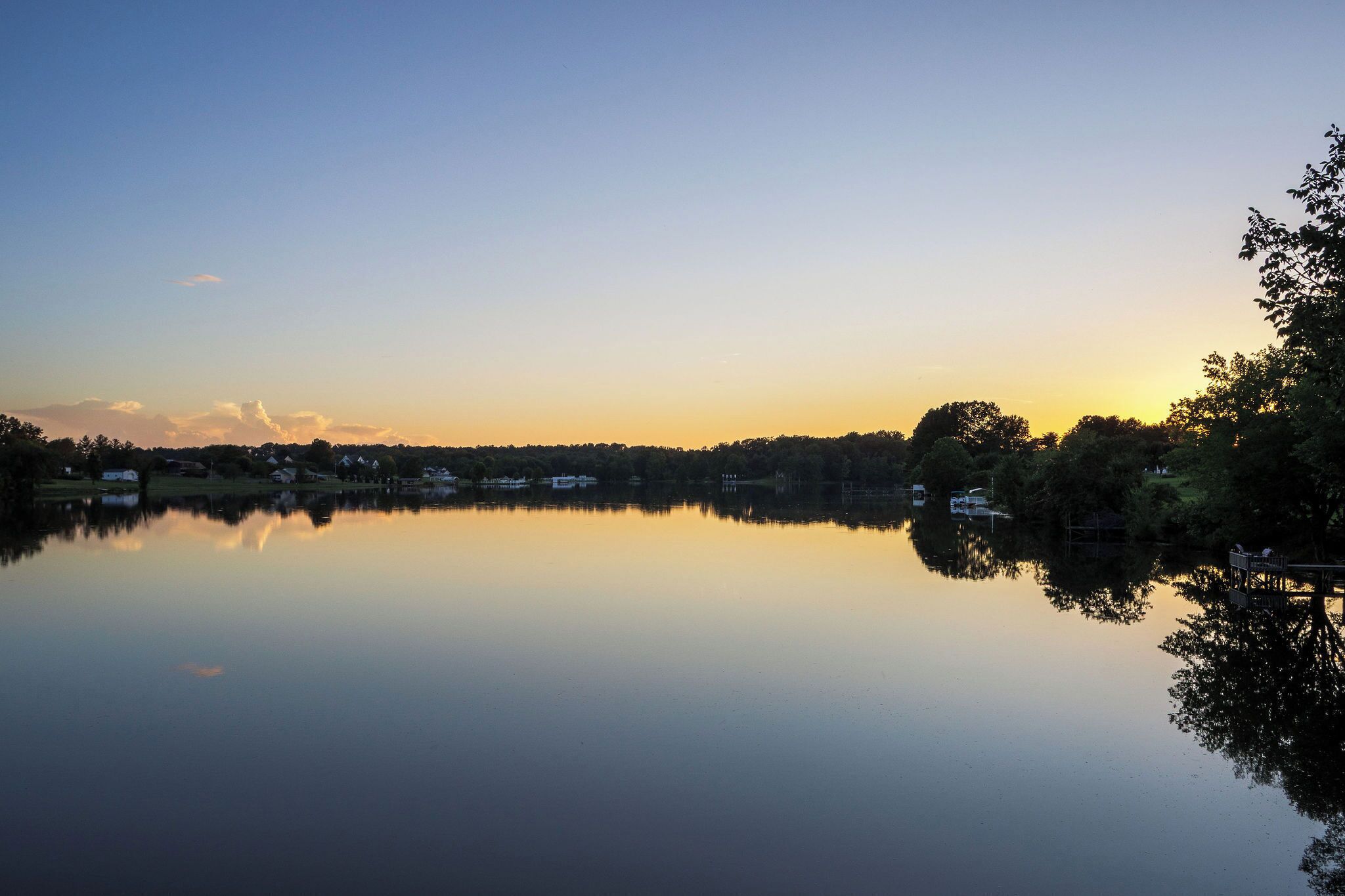 A calm lake with a clear sky, surrounded by trees and houses.