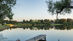 A serene lakeside scene with a wooden dock extending into the water, surrounded by lush greenery and a few buildings in the background. - Tiny House with lake view and large yard (McMinnville)