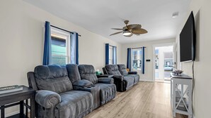 Ein Wohnzimmer mit einem Ecksofa, einem Deckenventilator und einem Fernseher an der Wand.