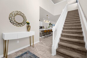 Un interior moderno con una escalera, una consola blanca con patas doradas y un espejo decorativo.