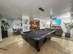 A pool table with a billiards ball, a television mounted on the wall, and a ceiling fan.