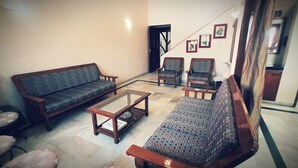 A living room with a sofa, two armchairs, a coffee table, and a patterned rug. - Aashvi Homes - 4BHK family friendly apartment (JAIPUR)