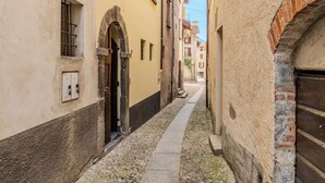 Une ruelle étroite pavée, bordée de bâtiments historiques dotés de portes en arc de cercle et d’un petit sentier.