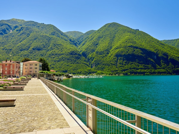 A waterfront promenade with a stone pathway, metal railing, and buildings in the background.