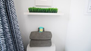 A bathroom with a white sink, a towel rack with a green plant, and a stack of towels.