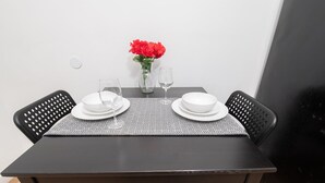 A dining table set with white plates, a wine glass, and a vase with red flowers.