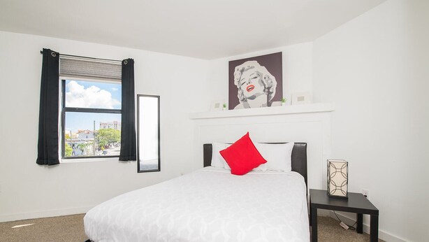 A hotel room with a bed, a nightstand, a lamp, a window with curtains, and a city view.