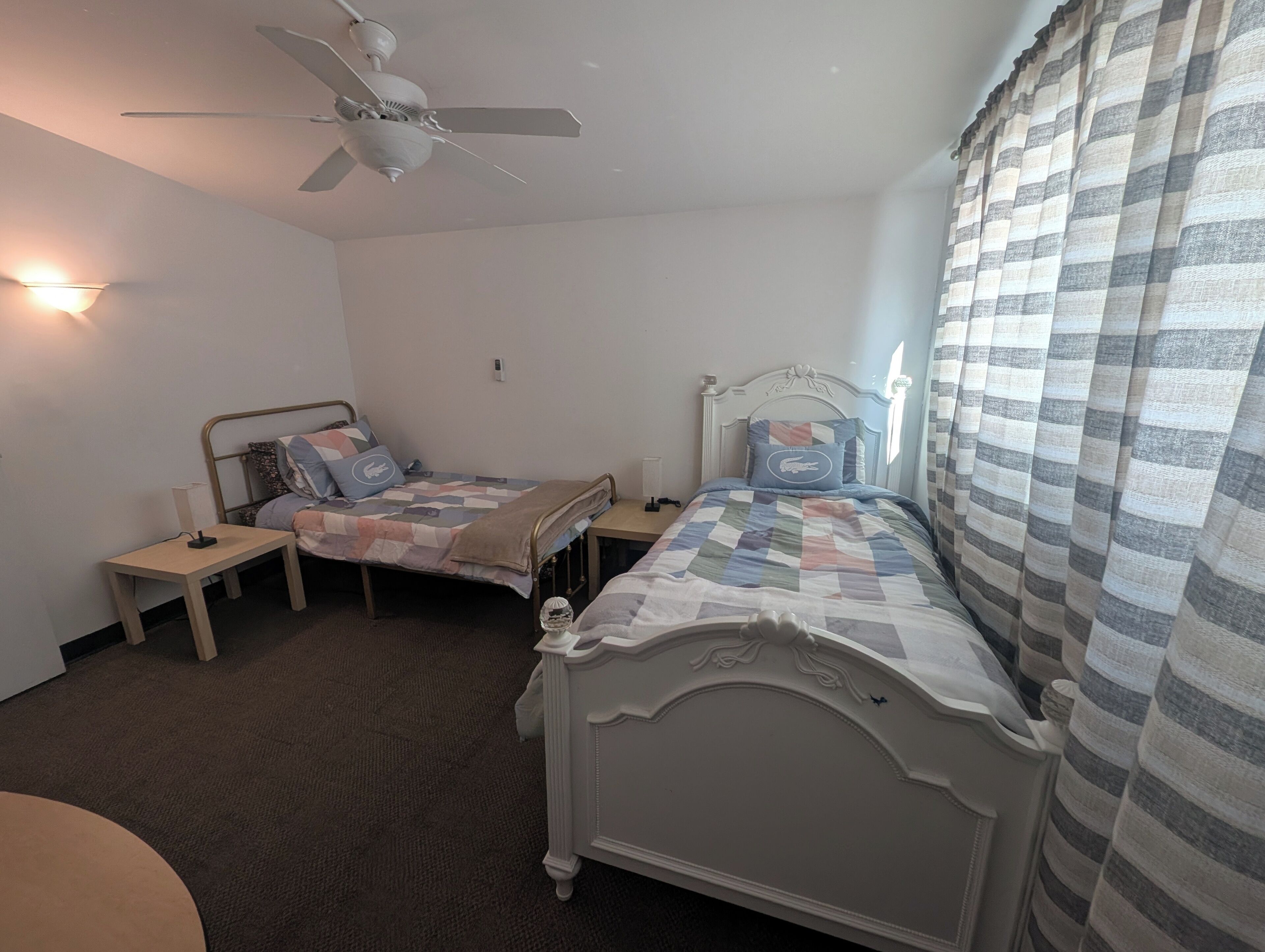 Un dormitorio con dos camas, un ventilador de techo y una ventana con cortinas.