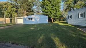 A mobile home with a small attached garage, a well-maintained lawn, and a tree in the background. - Near the park! 3-bedroom house with wifi and AC (White Pine)