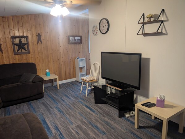 A living room with a dark brown sofa, a white chair, a television on a black stand, and a small table with a tissue box.