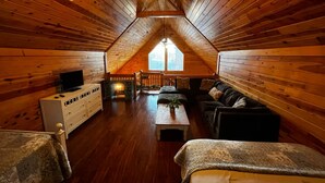 A cozy attic bedroom with wooden walls, a ceiling fan, a TV, a fireplace, a sofa, and a window. -  Washer dryer arcade game hot tub Waterview 3 bedroom 4 bed Awesome cabin.  (Sevierville)