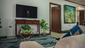 A living room with a flat-screen TV, a wooden cabinet, a potted plant, and a large painting on the wall.