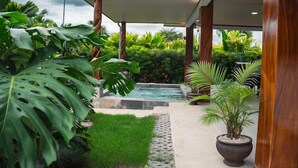 A modern house with a covered outdoor area, a small pool, and lush tropical plants.