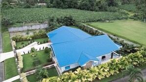 A house with a blue roof surrounded by lush greenery and a mountain in the background.