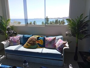 Un salón acogedor con vista al océano, un sofá estampado y dos plantas en macetas.