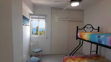 Une chambre avec un lit superposé, une chaise, une porte avec une clé, un ventilateur de plafond et une fenêtre donnant sur la mer.