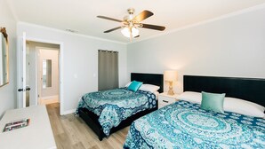 A hotel room with two beds, a ceiling fan, a nightstand with a lamp, and a desk with a chair.