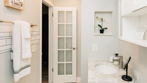 A bathroom with a white toilet, a marble sink, a glass door, and a towel rack with white towels.