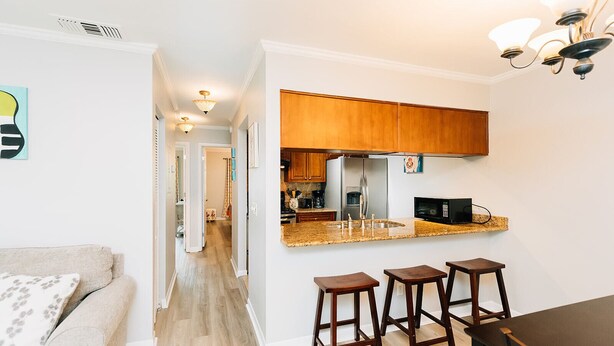 A modern kitchen with wooden cabinets, a stainless steel refrigerator, and a microwave. There are two wooden stools and a dining table.