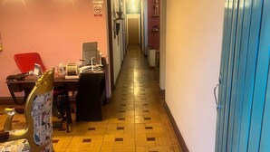 A hotel corridor with a patterned wooden floor, a dining area with a red chair and a table, and a blue door on the right. - Hotel casa Vecchia (Cali)