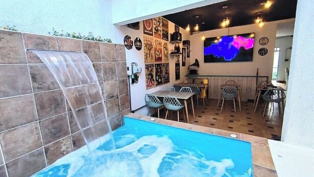 A hot tub with a waterfall feature, surrounded by a patio area with outdoor seating and a wall decorated with various posters and a large screen displaying a colorful image. - Hotel casa Vecchia (Cali)