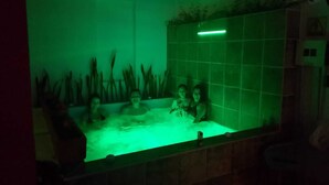 A bathtub with a green light, tiled walls, and a plant in the background. - Hotel casa Vecchia (Cali)