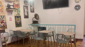 A dining area with a long wooden bench, several metal chairs, and a television mounted on the wall. - Hotel casa Vecchia (Cali)