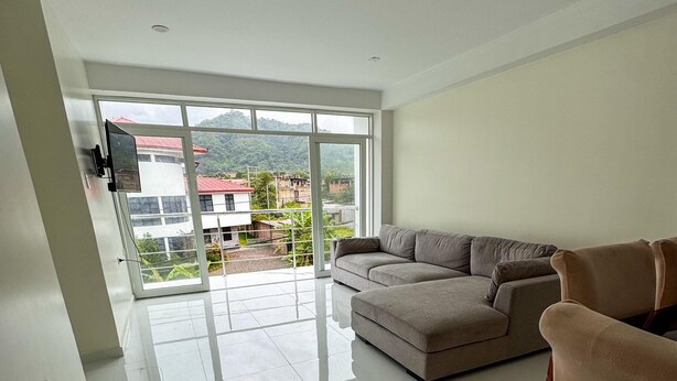 A modern living room with a large sectional sofa, a flat-screen TV mounted on the wall, and a sliding glass door leading to a balcony with a city view. - Amazing 4-bedroom third floor apartment in San Ramón (San Ramón)