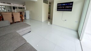 A modern living room with a grey sofa, a flat-screen TV mounted on the wall, and a dining area with chairs and a table. - Amazing 4-bedroom third floor apartment in San Ramón (San Ramón)